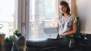 Woman working on iPad while sitting on the window sill
