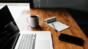 Laptop, phone, notebook, pen, and coffee mug on table